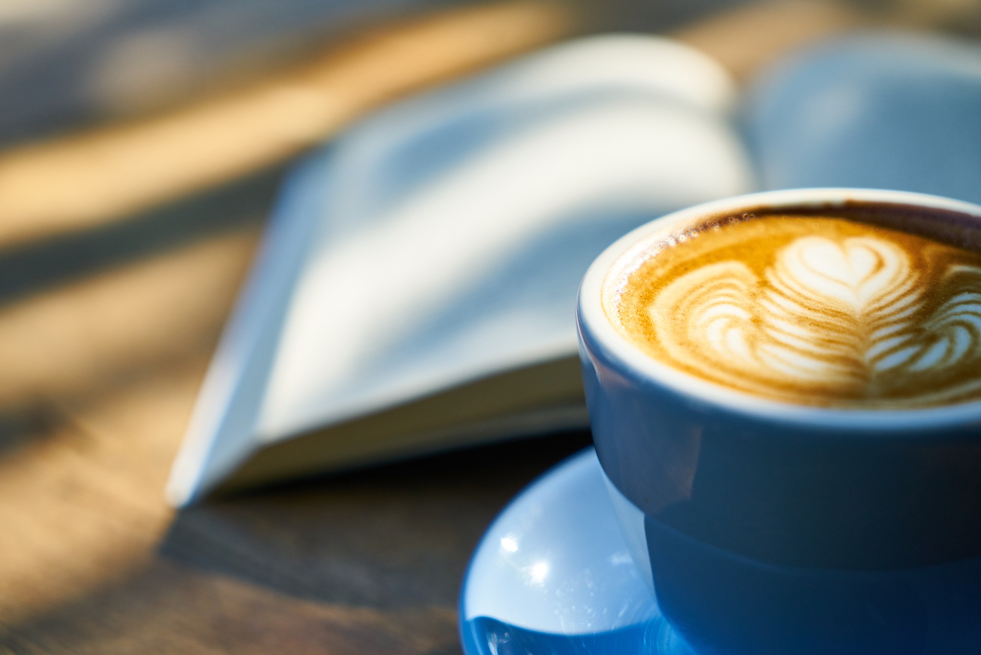 eine himmelblaue Tasse Cappuccino vor einem Buch im Sonnenlicht