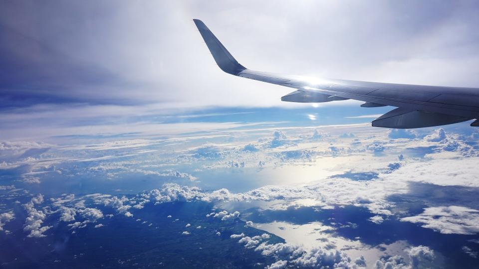 die linke Tragfläche eines Flugzeugs über den Wolken
