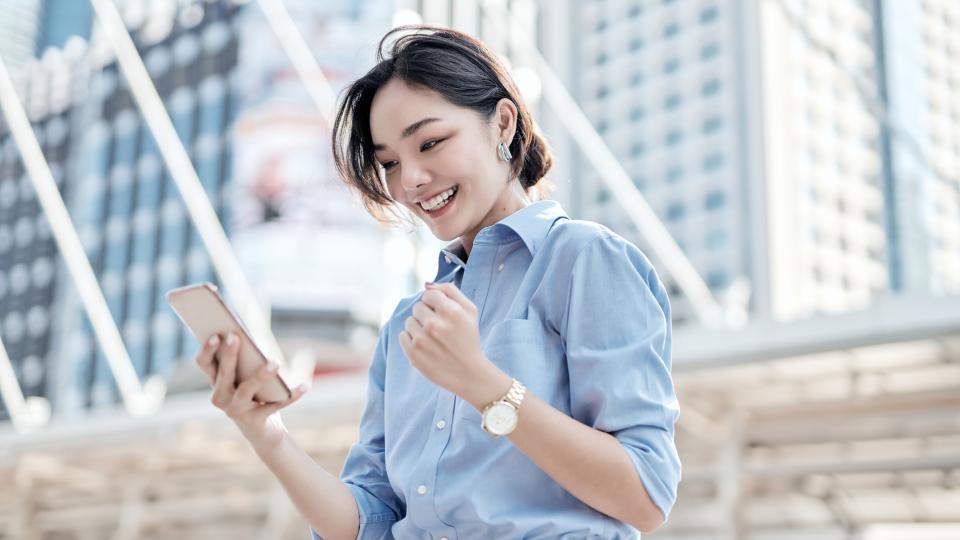 eine junge asiatische Frau, die lächelnd auf ihr Handy schaut und die Faust ballt