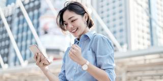 eine junge asiatische Frau, die lächelnd auf ihr Handy schaut und die Faust ballt